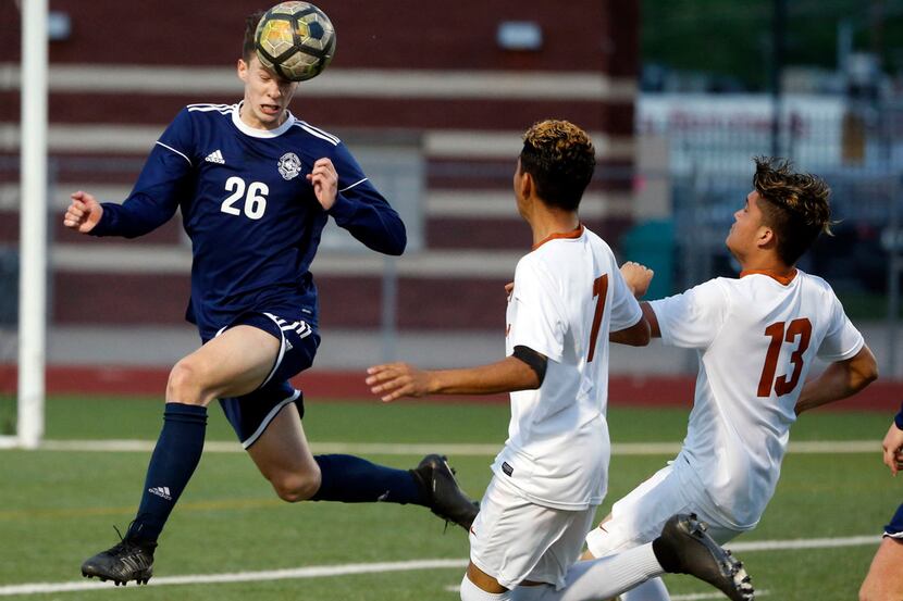 Flower Mound's Wyatt Brennan (26) heads the ball away from W.T. Whit's Angel Escorza (7) and...