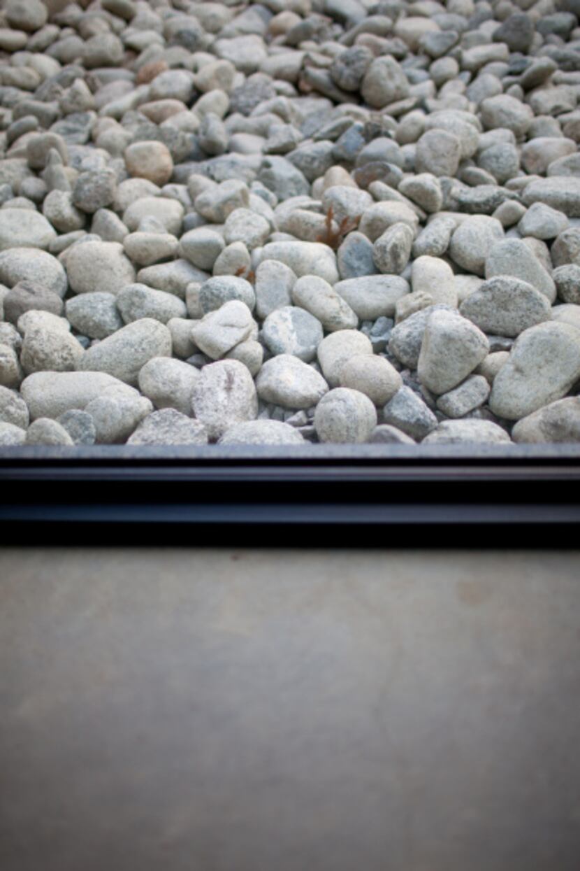 Glass separates the concrete-floor interior from the garden's tumbled rock.