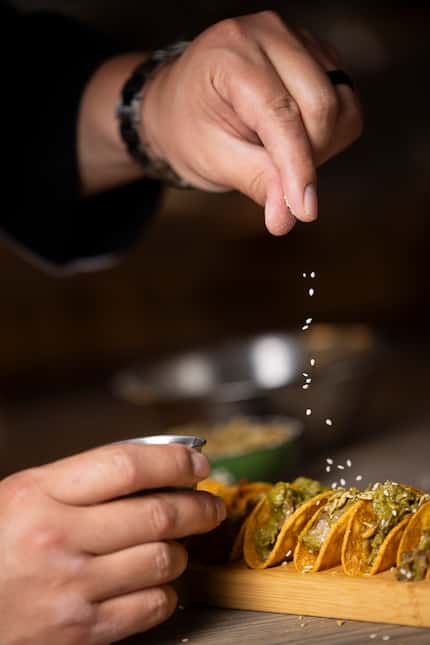 Culinary director Julian Rodarte sprinkles sesame seeds over Tejas’ new duck tacos with mole.