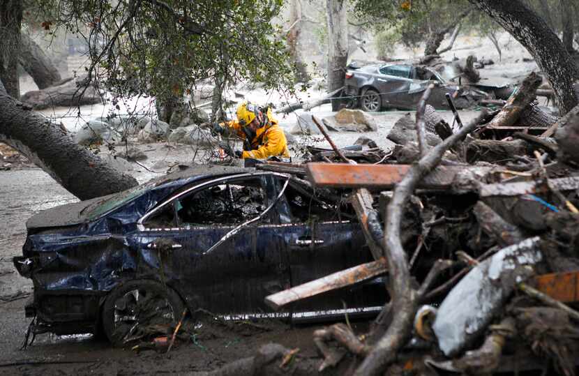 A member of the Long Beach Search and Rescue team looks for survivors in a car in Montecito,...