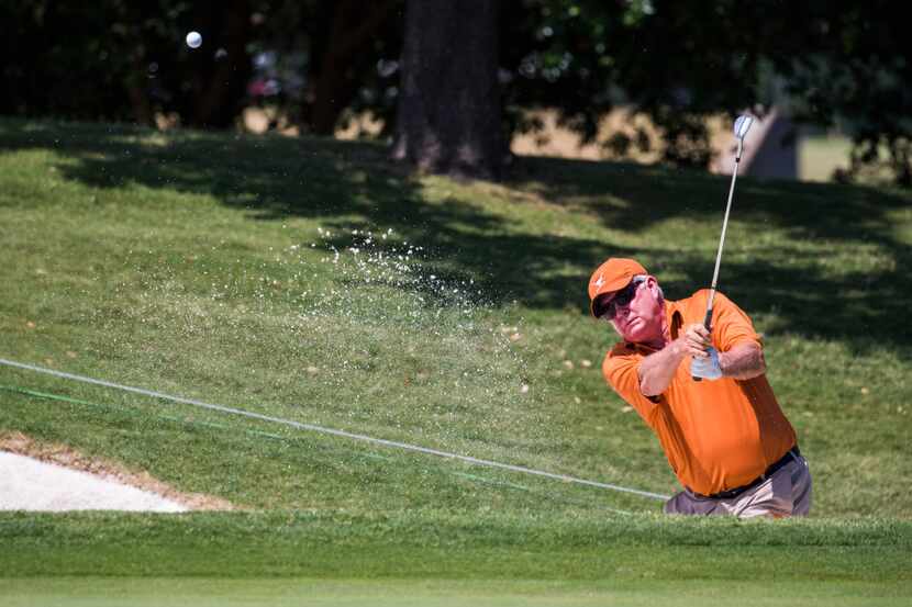 Former University of Texas football coach Mack Brown hits a ball out of the sand toward the...