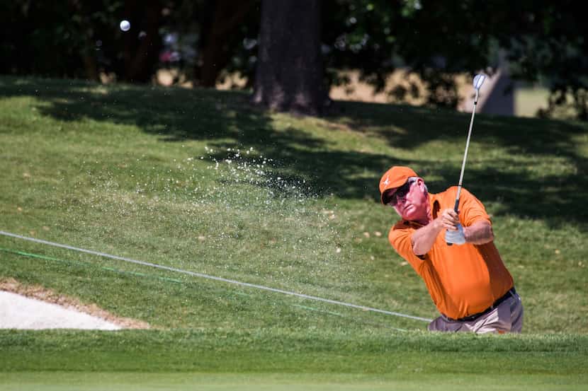 Former University of Texas football coach Mack Brown hits a ball out of the sand toward the...