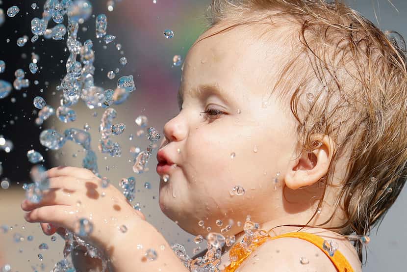 Linden Mead, 1, reacts as she tries to taste water drops sprayed from a fountain, on Friday,...