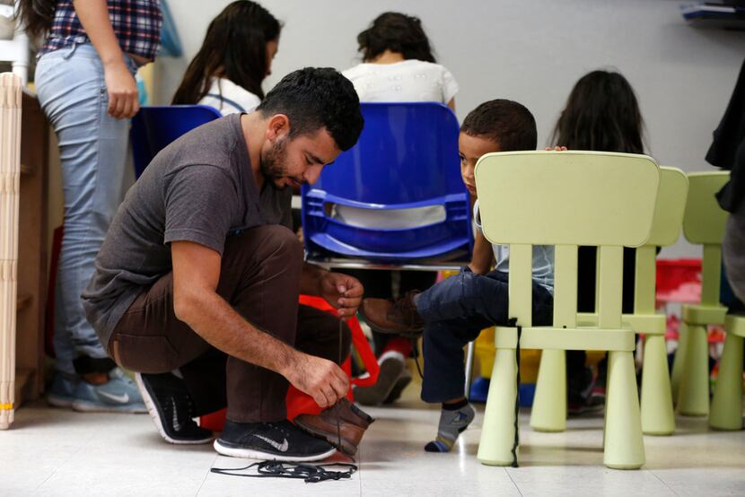An immigrant puts shoelaces back on his child's shoes at the Humanitarian Respite Center in...