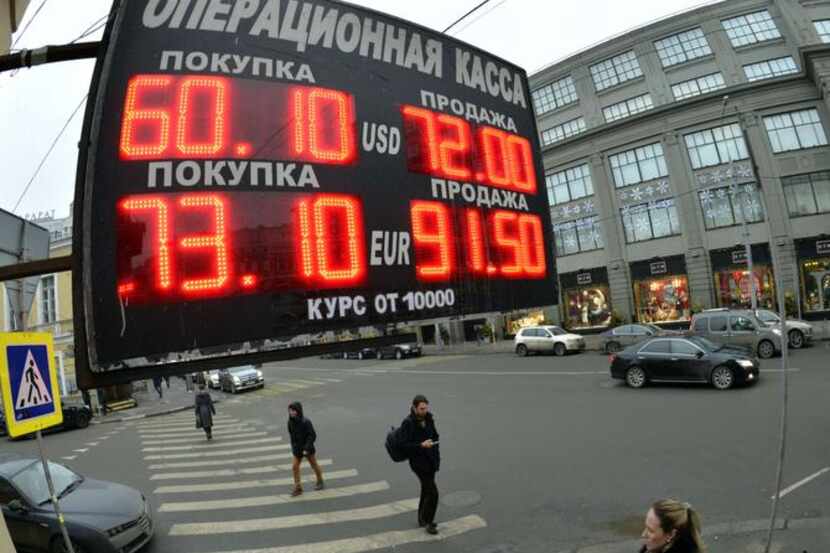 
Pedestrians walk under a board listing foreign currency rates against the Russian ruble...