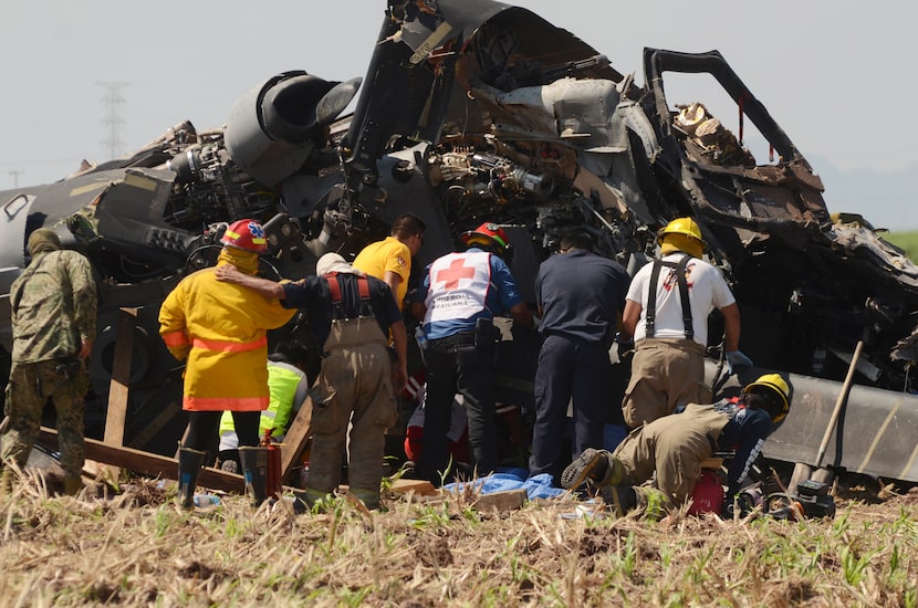 Emergency personnel work next to a navy Blackhawk helicopter crashed after supporting those...