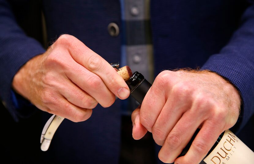 James Tidwell removes the cork from a wine bottle.