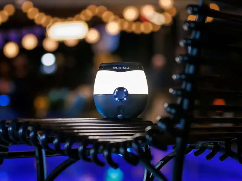 Mosquito control device sitting on a black patio chair near a pool and string lights