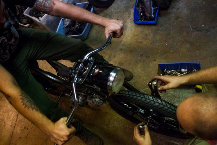 
Josh Lacheney, left, steadies a moped while Kyle Salter works on the wheel at Kyle's...