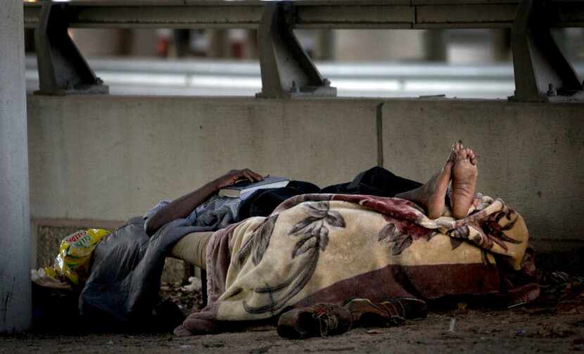 A man lays on a cot alongside I-45 near a homeless encampment. 