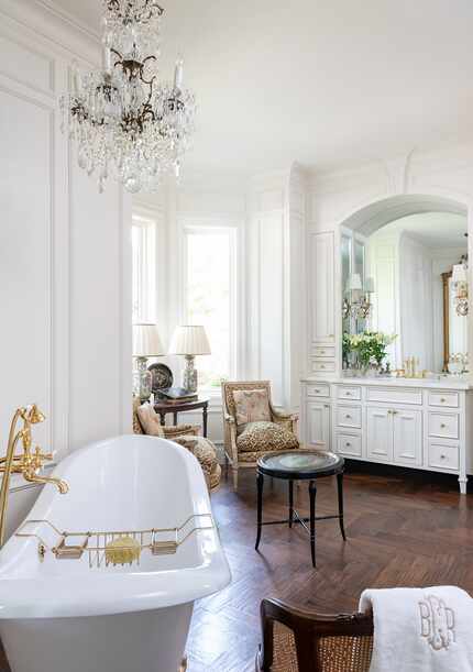 White bathroom with dark wood floors, antique chairs near windows and white freestanding tub