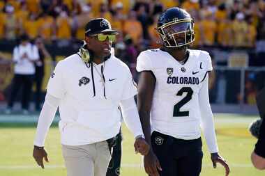 Colorado head coach Deion Sanders (left) talks with his son and starting quarterback Shedeur...