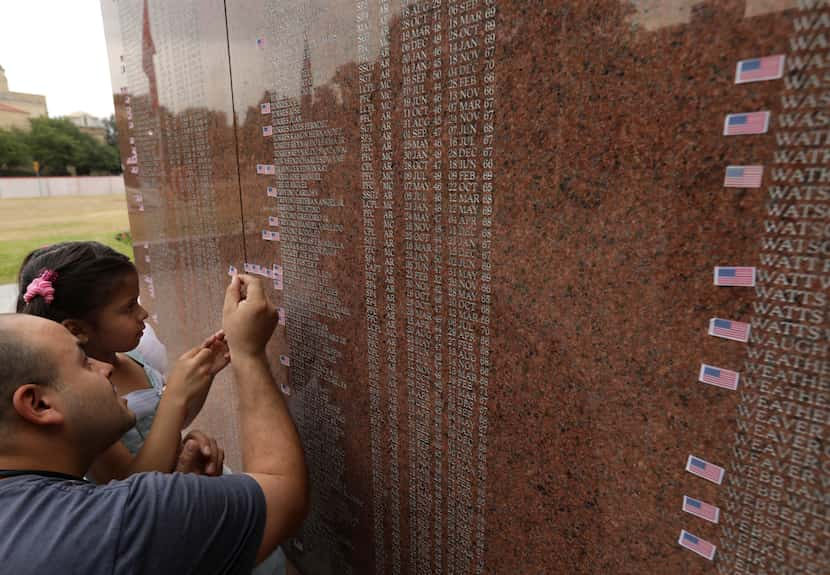 Omar Bravo and 6-year-old Caroline Bravo place a memorial flag sticker on one of the names...