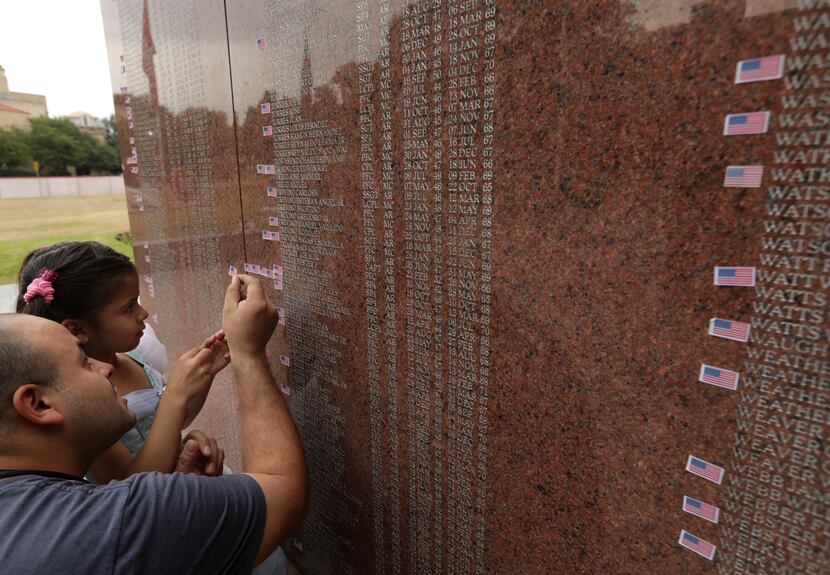 Omar Bravo and 6-year-old Caroline Bravo place a memorial flag sticker on one of the names...