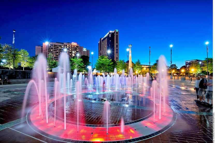 Foto de una plaza con fuentes y luces rojas y azules.