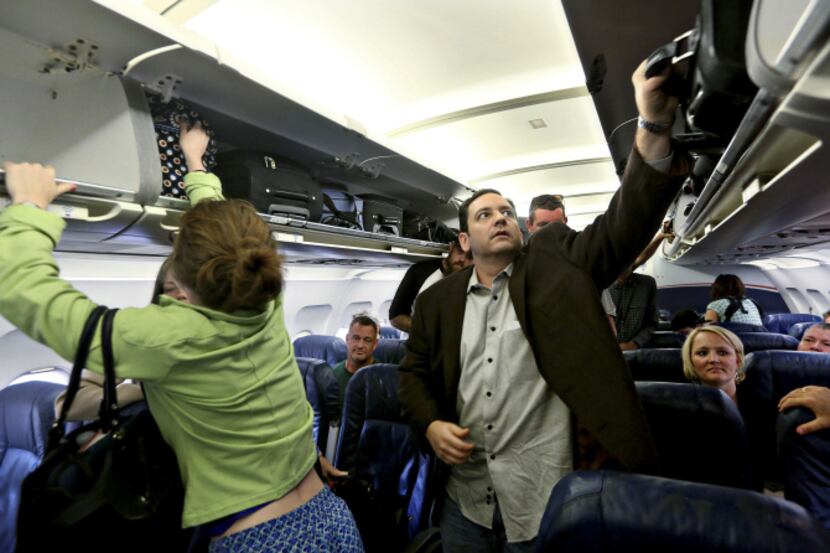 Passengers aboard a US Airways flight take their baggage from overhead bins as they depart...