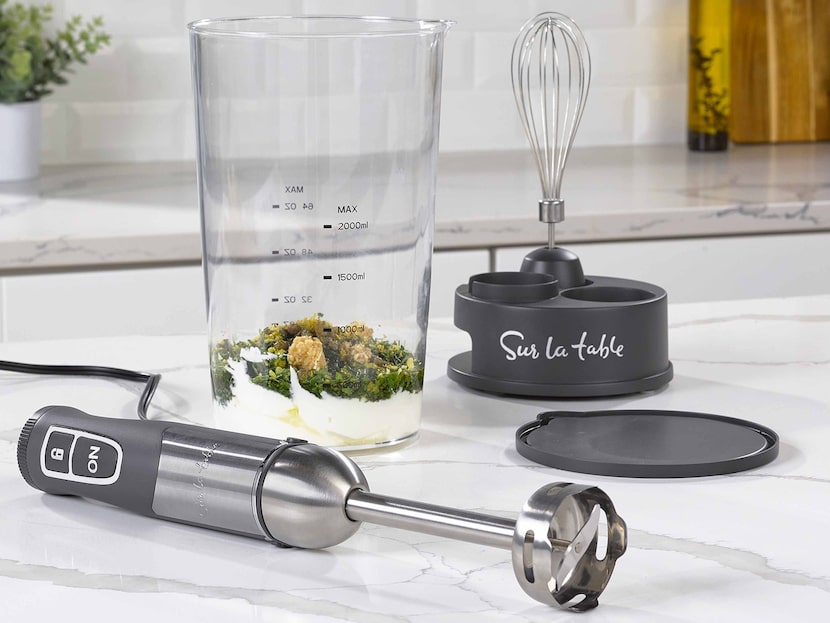 Handheld immersion blender on a white counter with whisk and stand