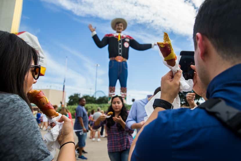 Fairgoers eat Fletcher's Corny Dogs while taking photos of Big Tex at the State Fair of...