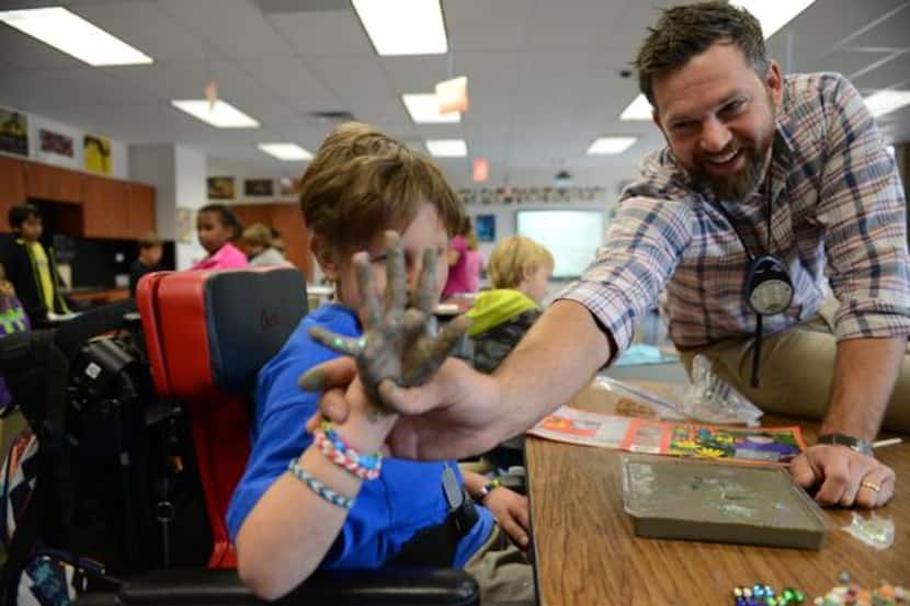 
Art teacher Justin Preston helps Kyle Murray, 10, dip his hand into concrete to make his...