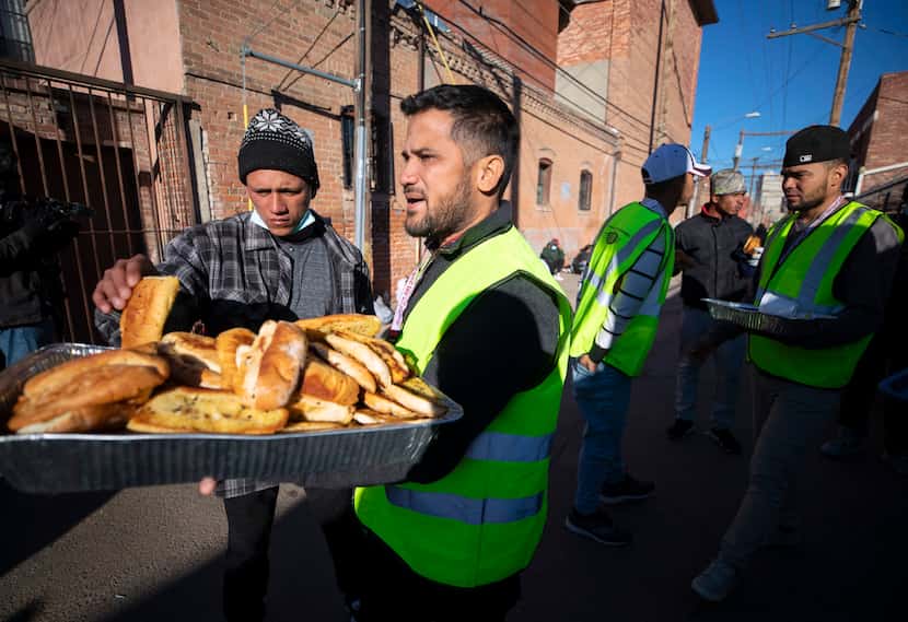 Church volunteers serve garlic bread to migrants camping outside the Sacred Heart Church in...