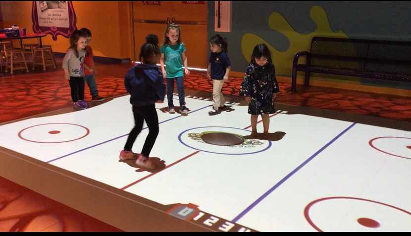 Kids play a game of air hockey in the Stomp and Play station during the grand opening of the...