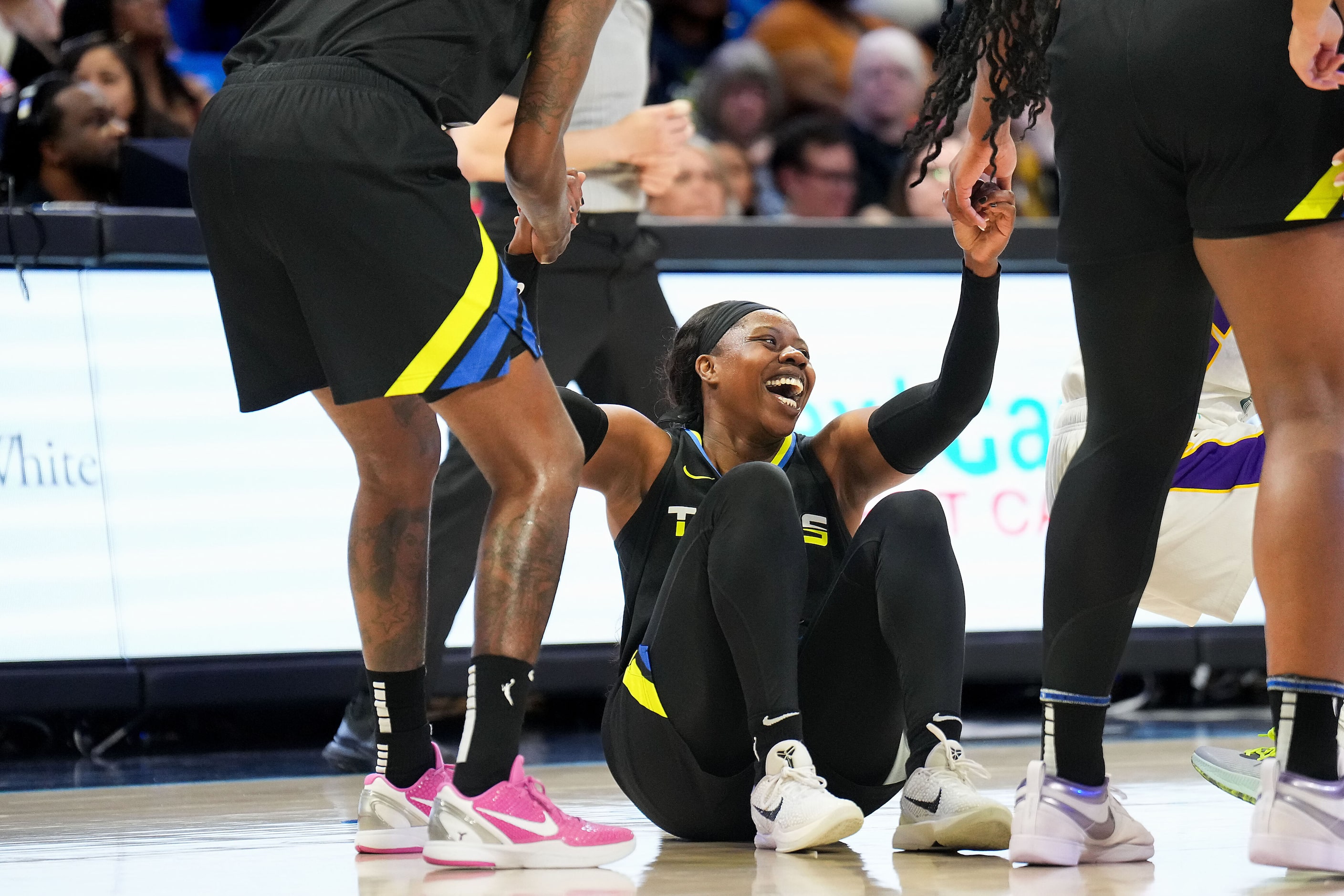 Dallas Wings guard Arike Ogunbowale laughs as she gets help off the floor after chasing a...