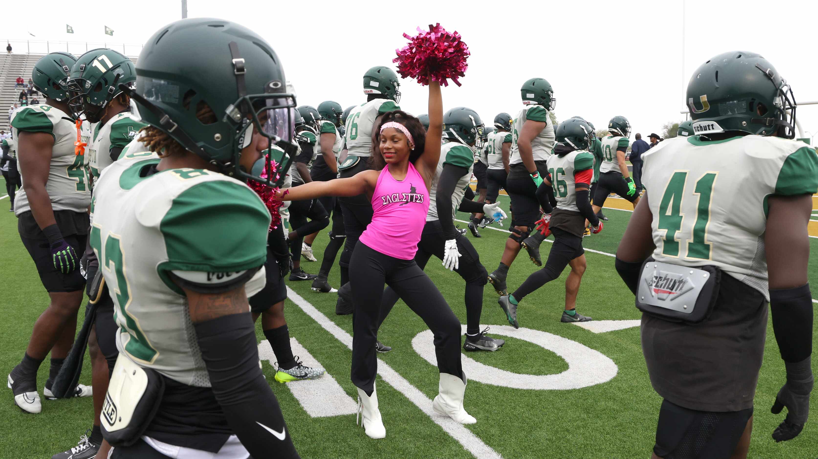 A member of the DeSoto Eaglettes is framed by Eagles football players as they warm-up just...