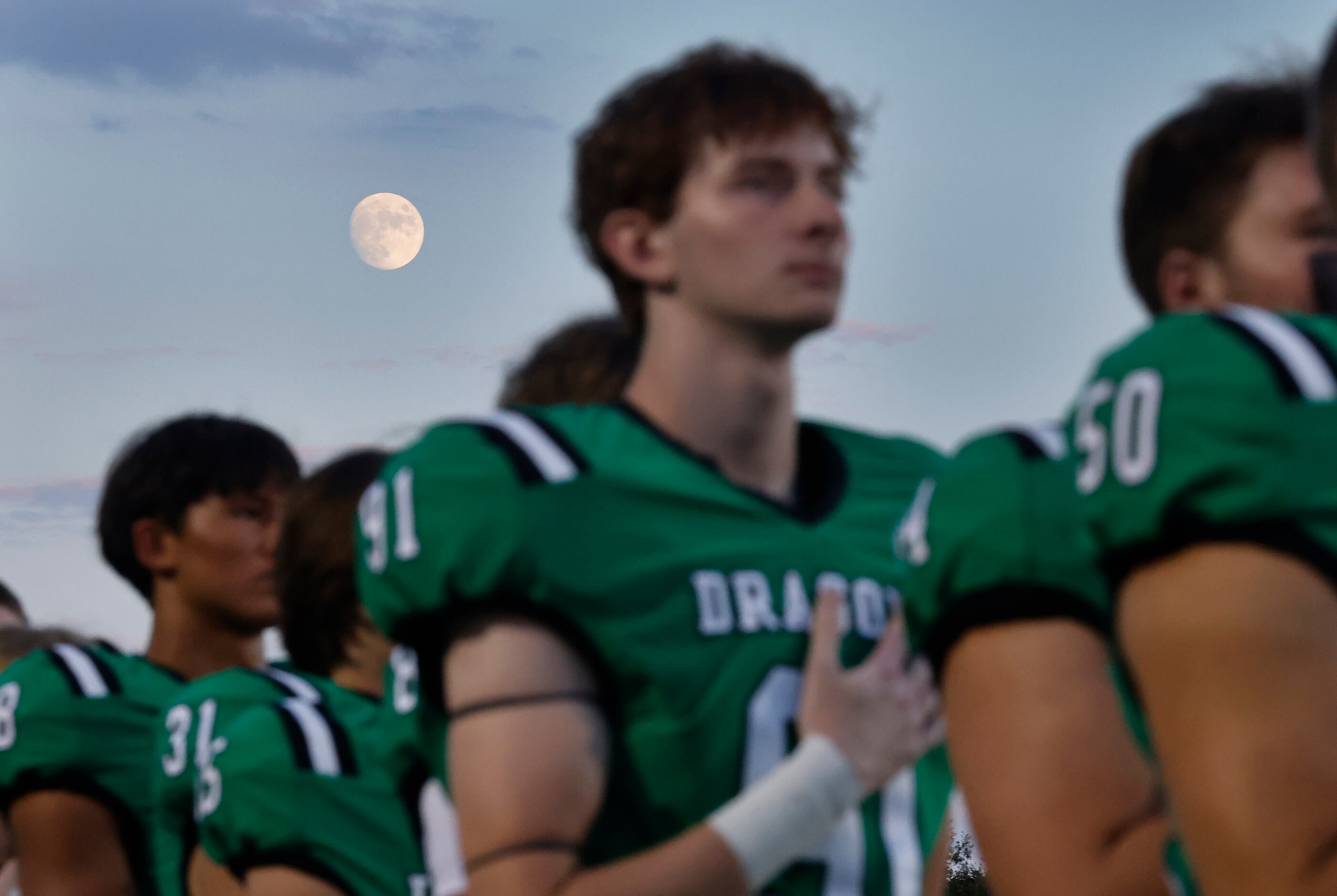 A nearly full moon rises behind Southlake Carroll  football players who stand for the...