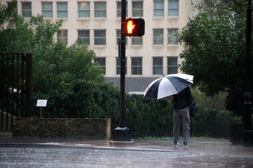 A person waits to cross the street as they endure wet and cold conditions  Monday.