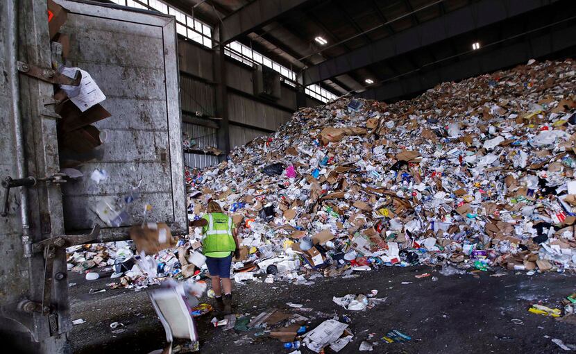 A trailer door is opened on a truck filled with unsorted recyclable trash as it is offloaded...