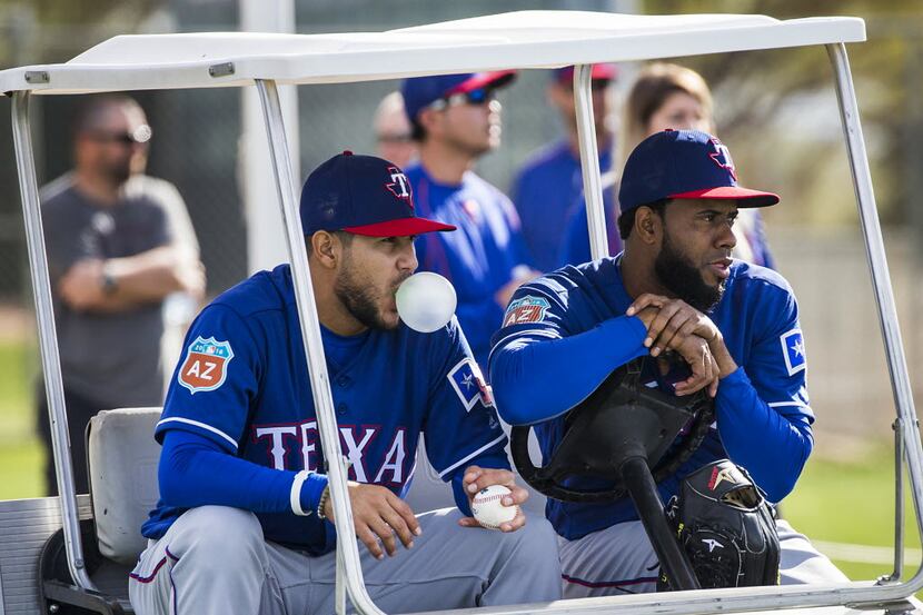 Texas Rangers pitcher Martin Perez blows a bubble while sitting in a cart with Yohander...