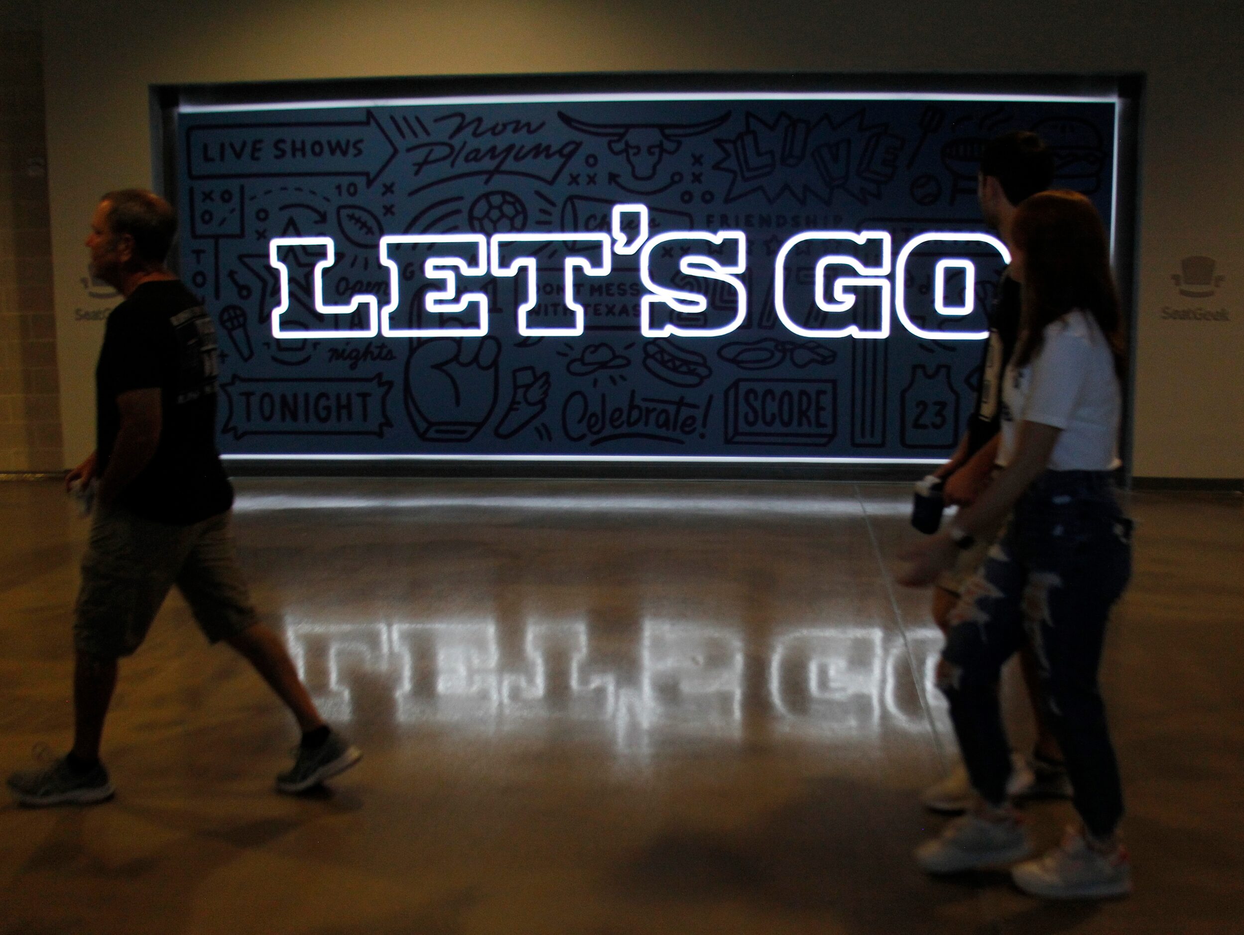 Dallas Cowboys fans walk past an illuminated sign as they make their way to seats to watch a...