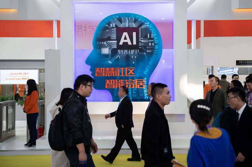 Visitors walk past a stand with artificial inteligence security cameras using facial...
