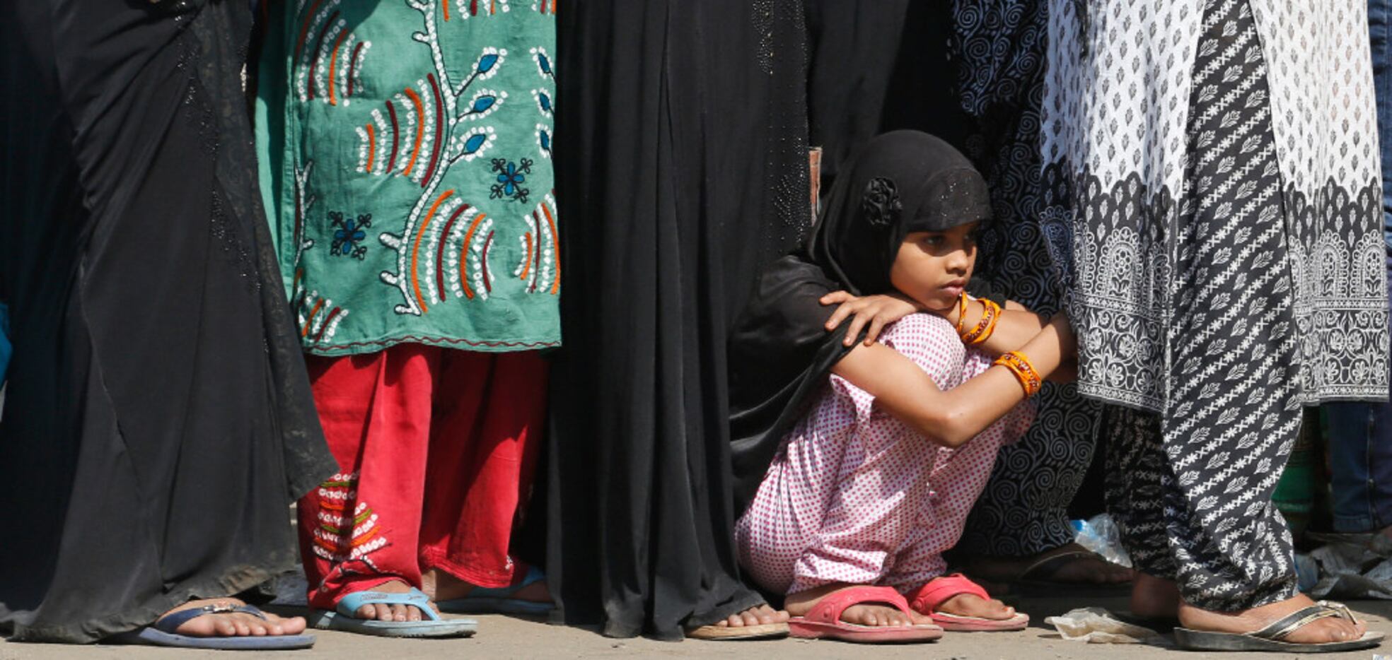 An Indian girl rests as she waits in a queue with elders standing to deposit and exchange...