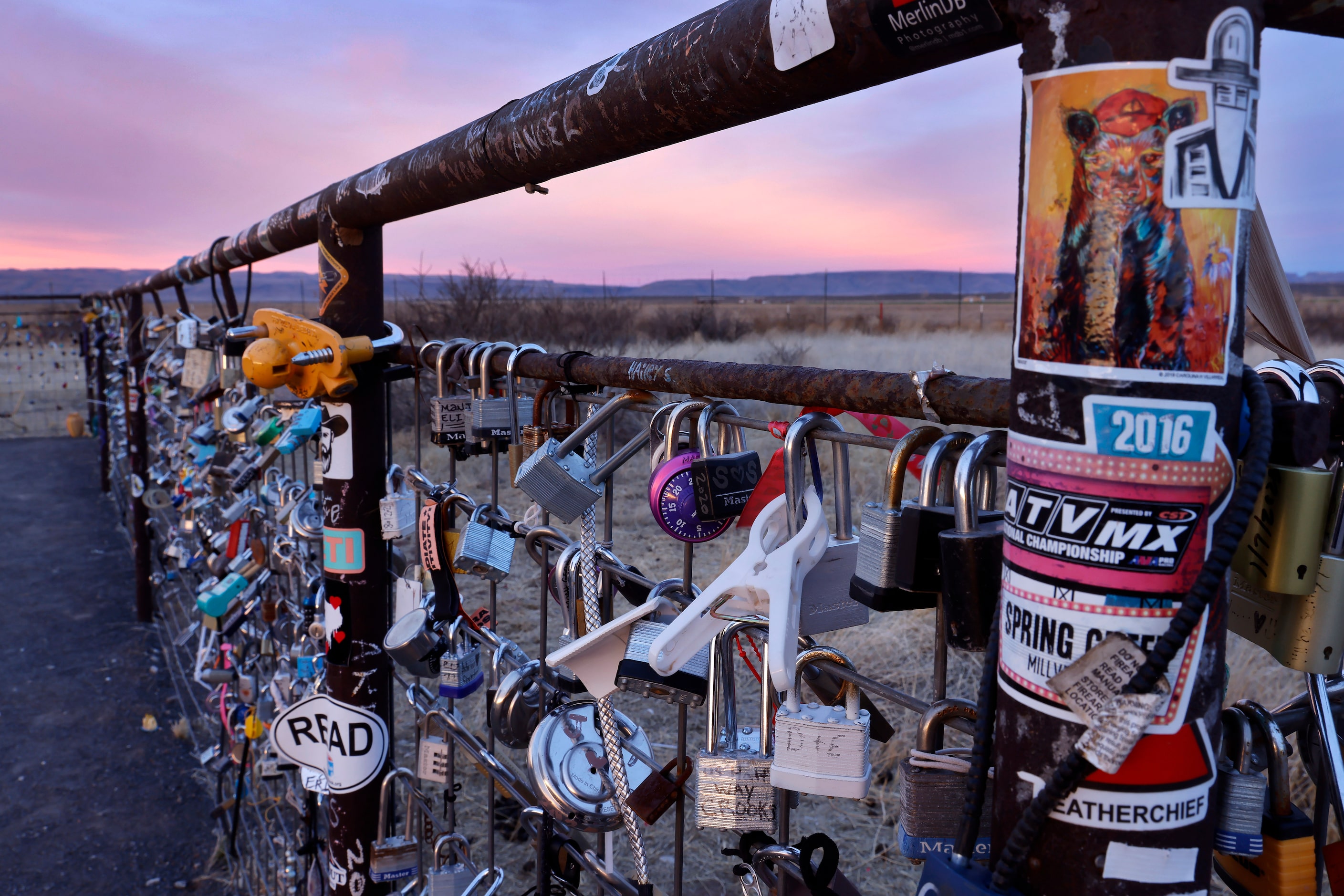 The skies turn pink and blue behind a fence full of love locks, similar to the famous Pont...