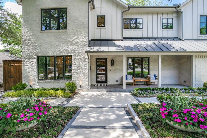 A white two-story home features purple floral arrangements in the front yard.