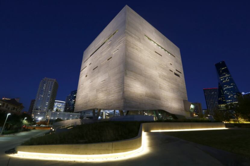 An illuminated sidewalk on the west side of the Perot Museum of Nature and Science leads...