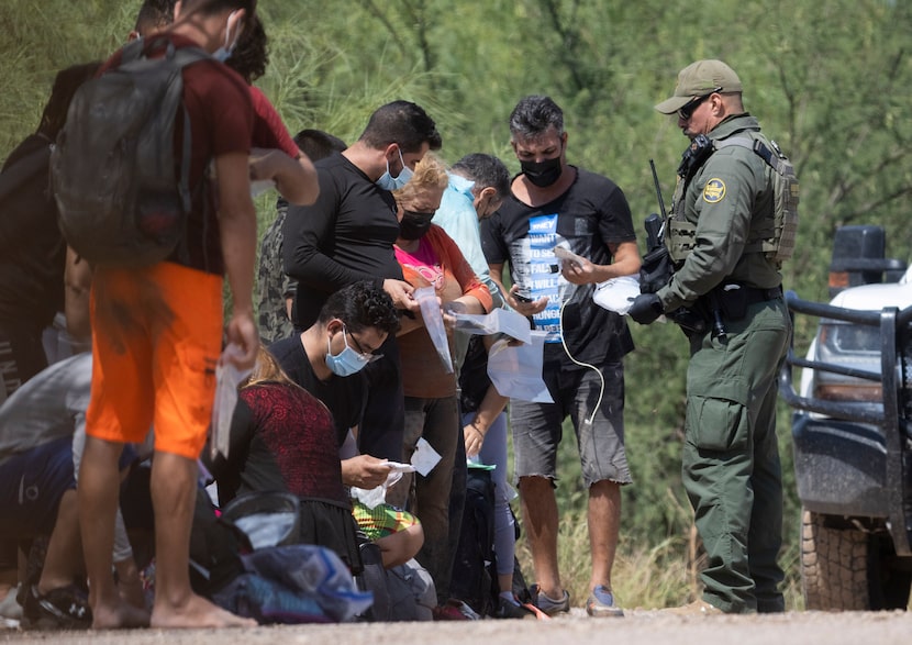 A group of mostly Cuban migrants are handed bags for their belongings by Border Patrol...