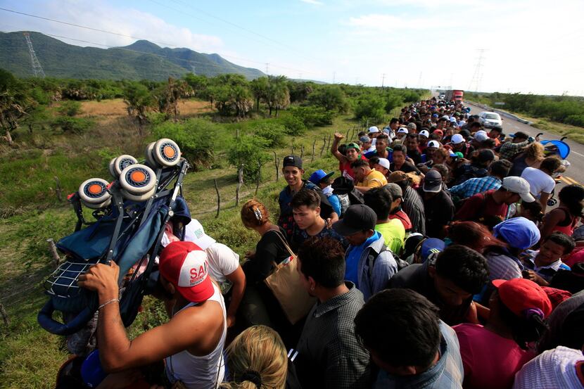 A man holds up a stroller as hundreds of migrants hitching a ride accommodate themselves on...
