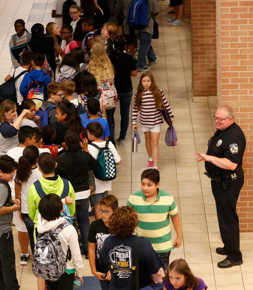 McKinney police senior resource officer Chris Golden waves at students as they make their...