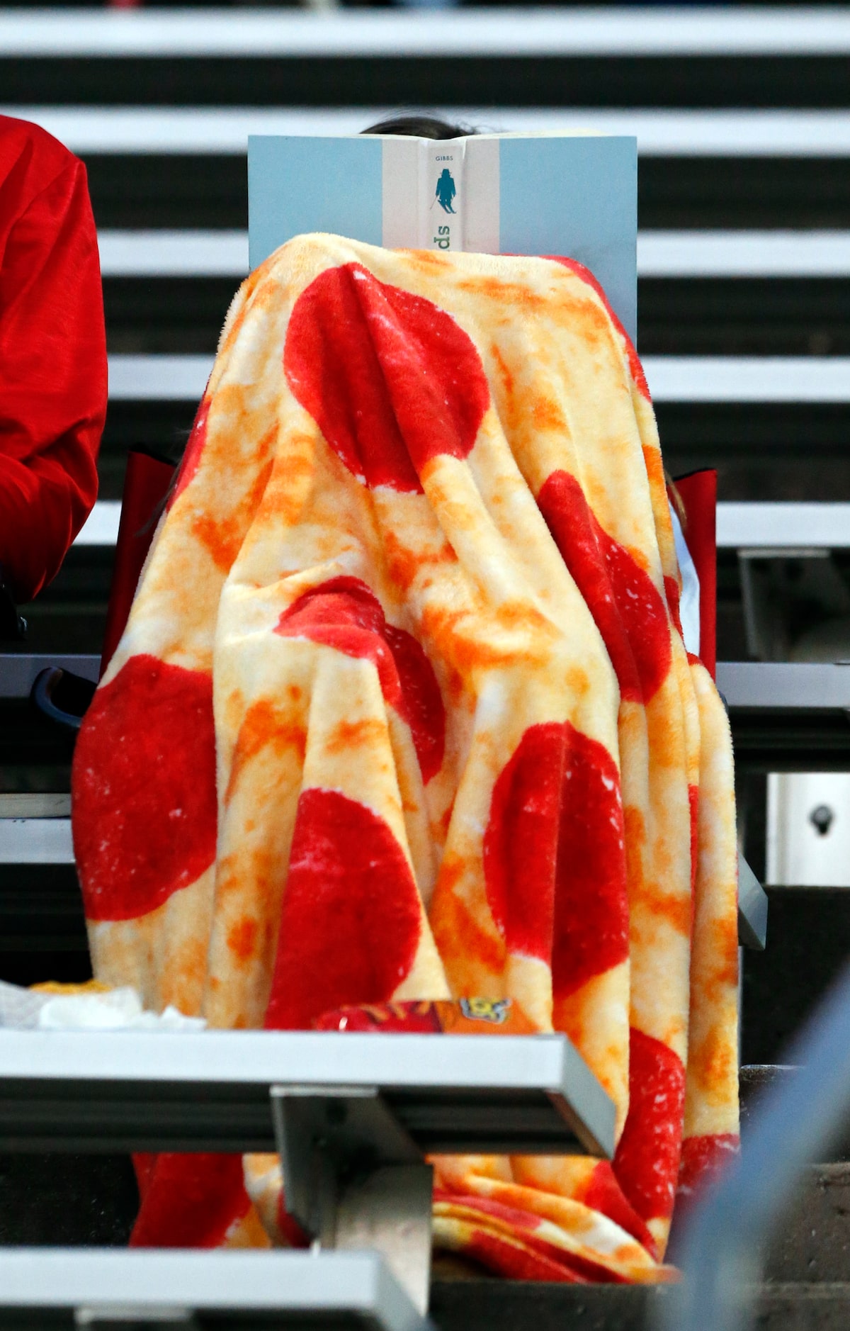 A Woodrow Wilson High fan reads a book covered with a pizza-themed blanket during the first...