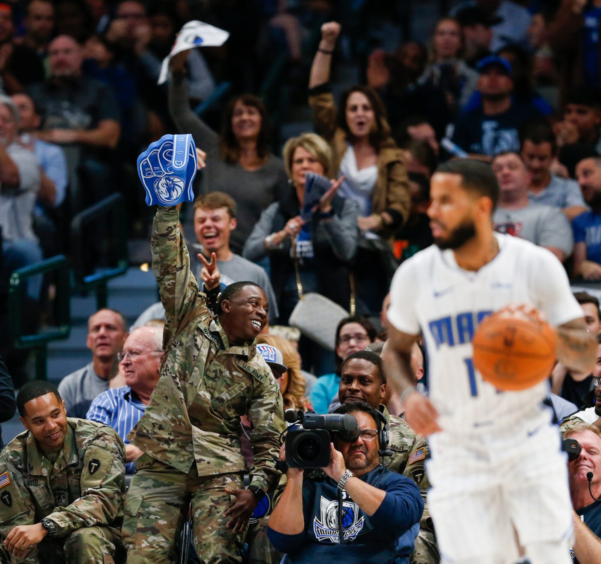 Armed forces members celebrate from the sidelines during the third quarter of an NBA game...