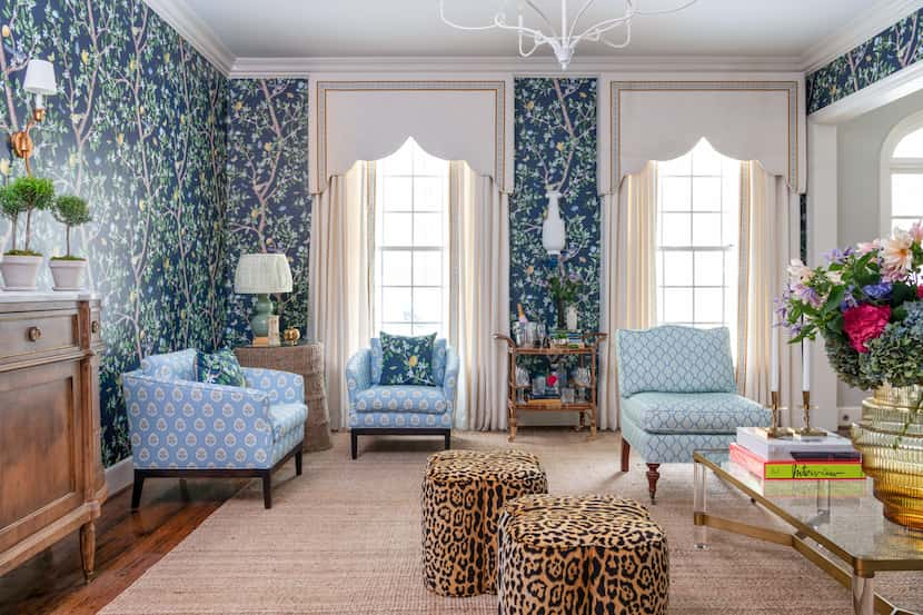 Walls in a living room are covered in a patterned wallpaper and cornices and drapes cover...