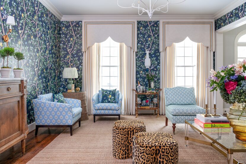 Walls in a living room are covered in a patterned wallpaper and cornices and drapes cover...