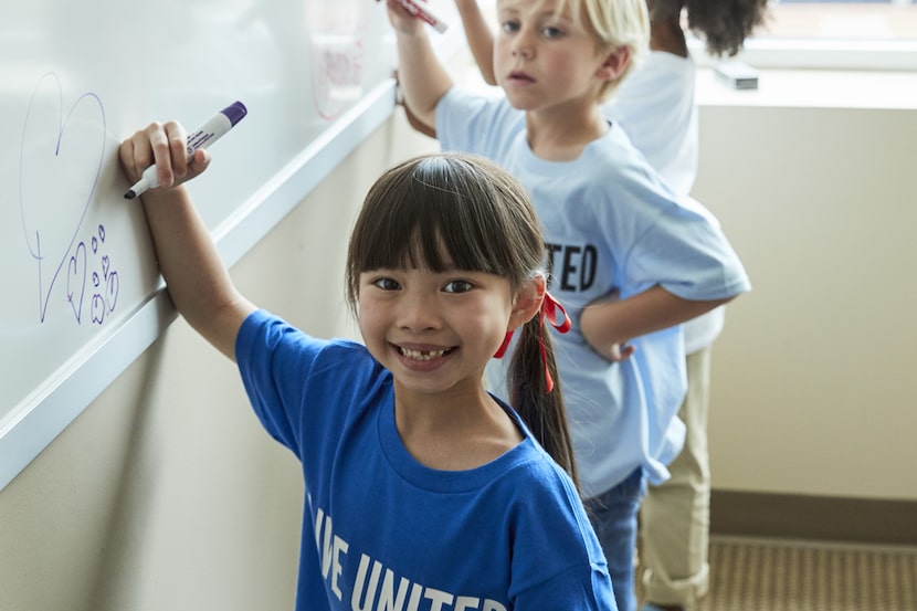 Children write on a whiteboard in a classroom.