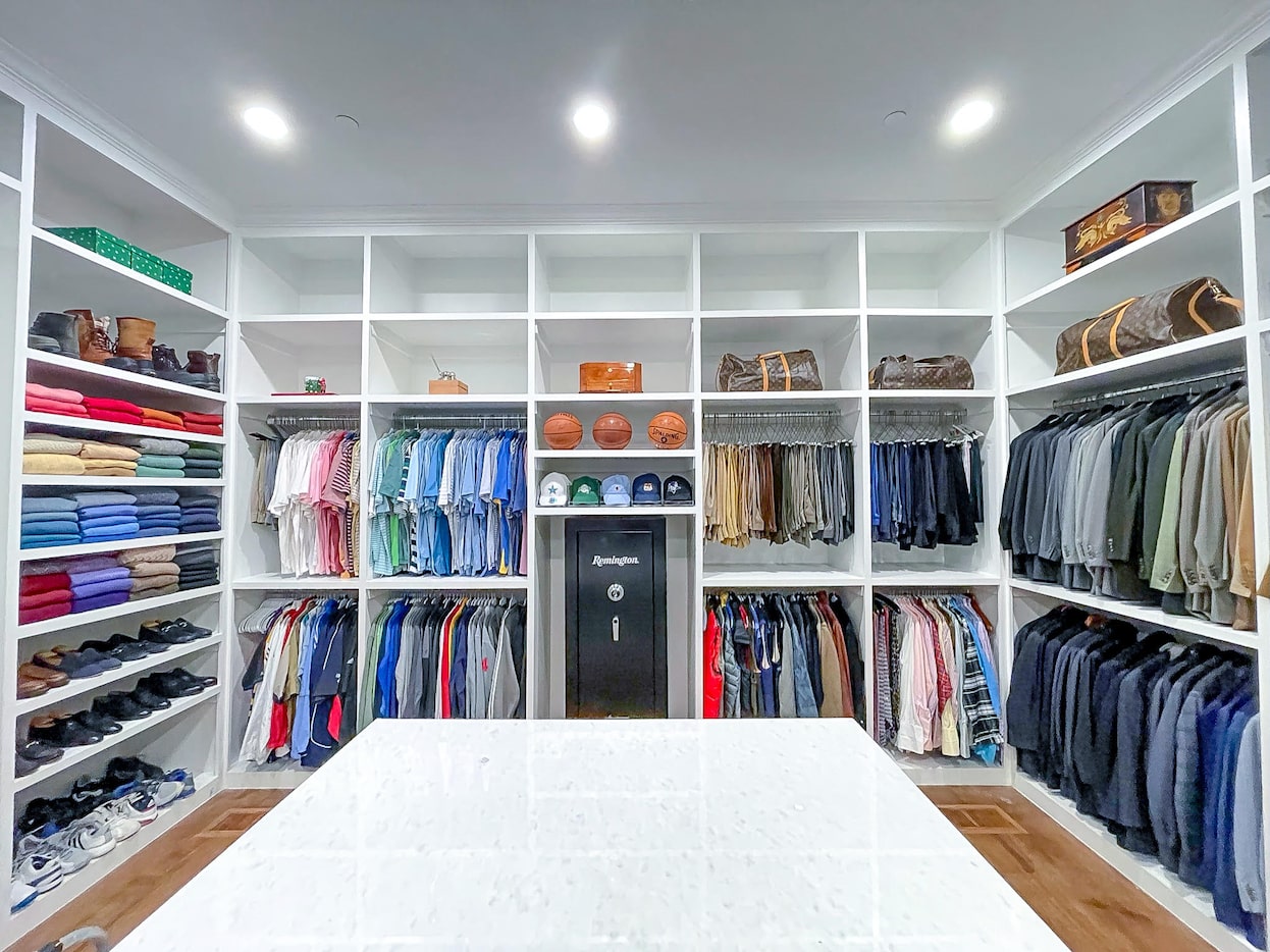 A men's closet which is organized with jackets, shirts, pants, and shoes.