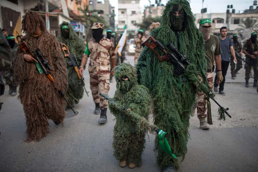  A masked Palestinian boy walks in a parade with members of the Izzedine al-Qassam Brigades,...