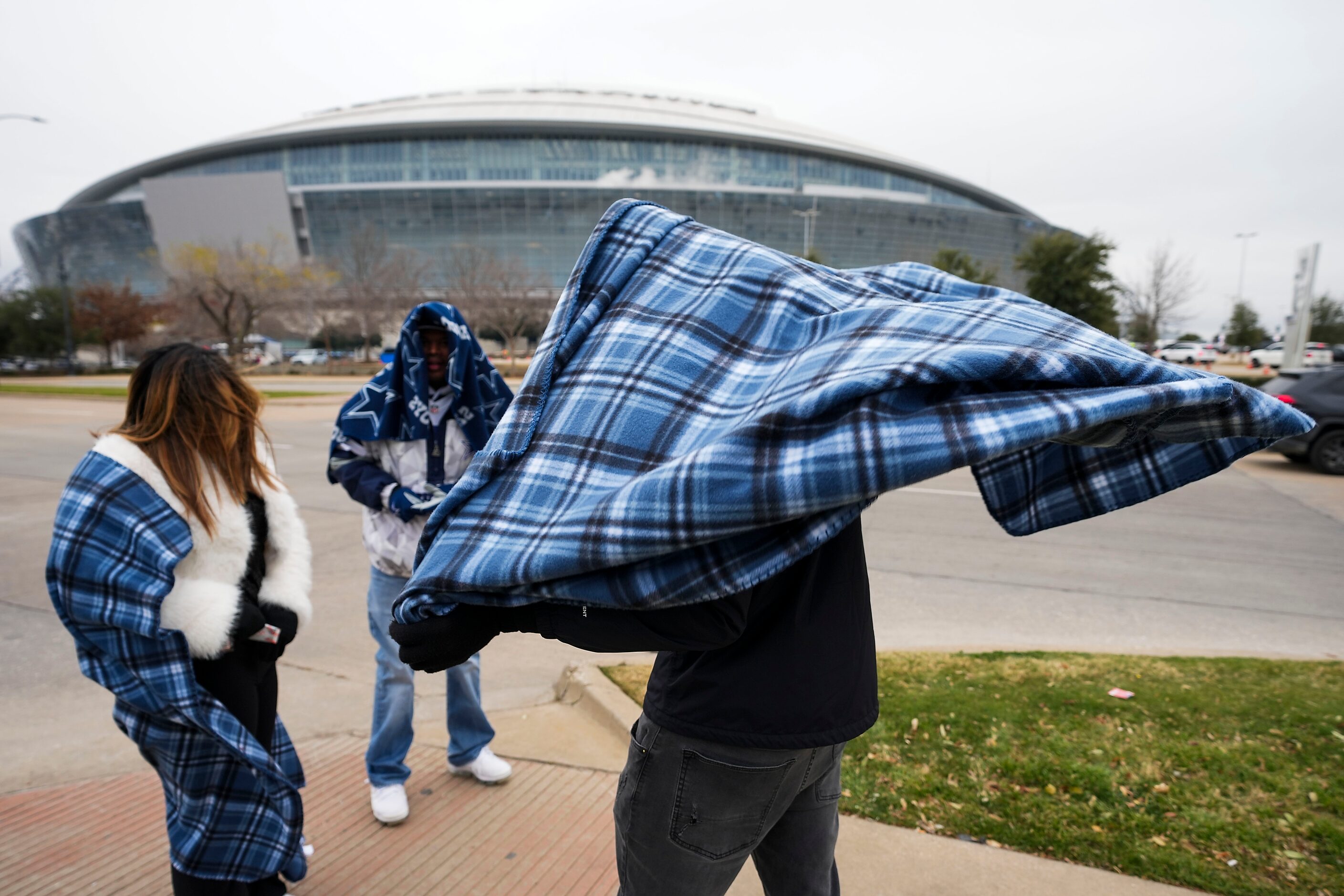 Dallas Cowboys fans Luke Ortiz tries to hold onto his blanket in the wind as he bundles up...