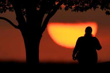 Una mujer mira la puesta del sol en un día cálido, el 20 de agosto de 2023 en Kansas City,...