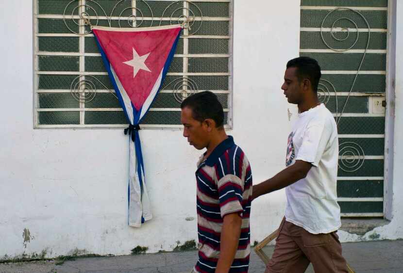People passed a Cuban flag gathered with a black ribbon, a sign of mourning, in the town of...